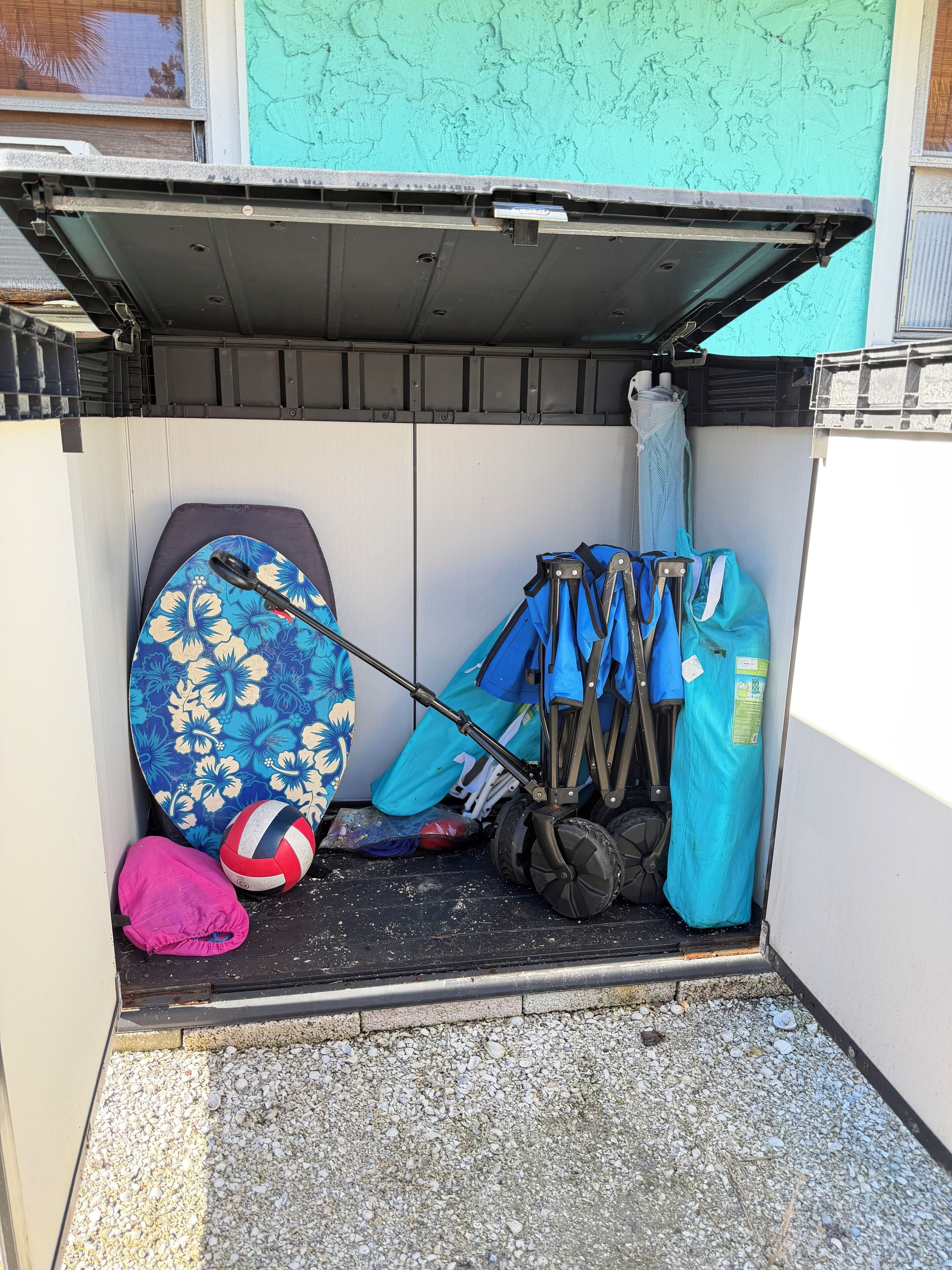 A compact storage area with a surfboard, a volleyball, a blue bag, and a pair of shoes.