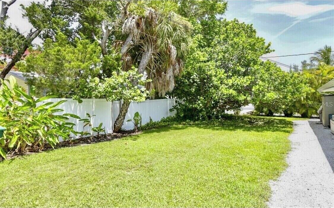 A well-maintained grassy yard with a white fence and various trees, including a palm tree.