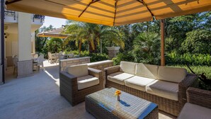 Un patio al aire libre con mobiliario de mimbre, una mesa de centro de vidrio y una sombrilla amarilla que da sombra.