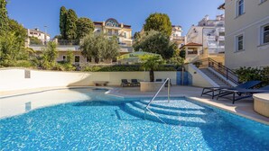 Una piscina con un deck de baldosas, sillas de descanso y una escalera que conduce a un nivel superior.