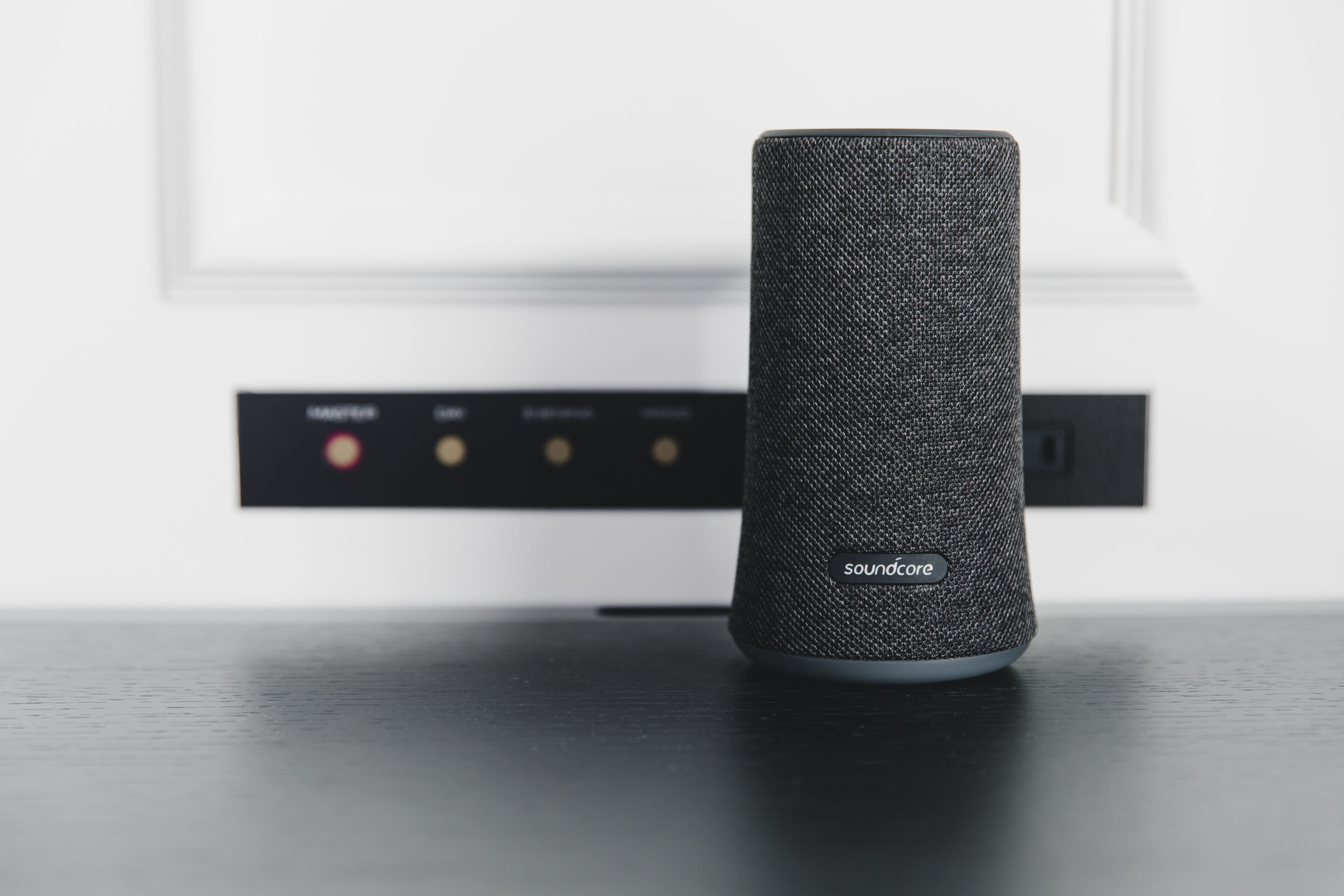 A smart speaker on a table with a control panel in the background.