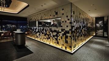 A modern hotel lobby with a unique geometric wall design, a reception desk, and a view of the cityscape through large windows.