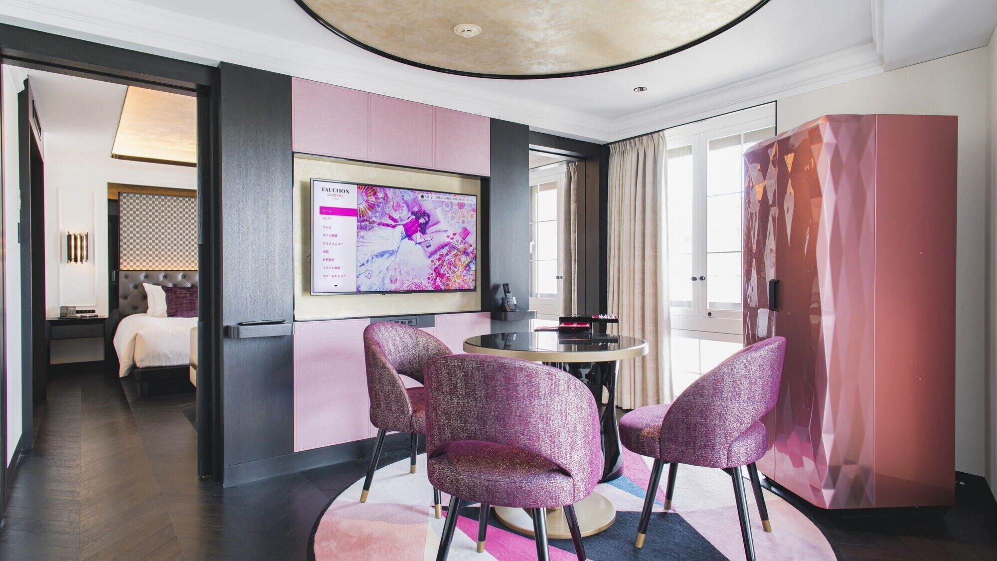 Habitación de hotel con cama, escritorio, televisión y pared rosa.
