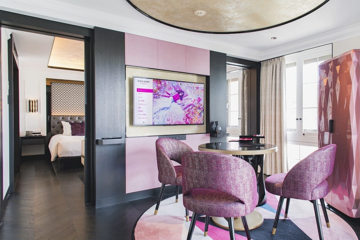 A hotel room with a bed, a desk, a TV, and a pink wall.