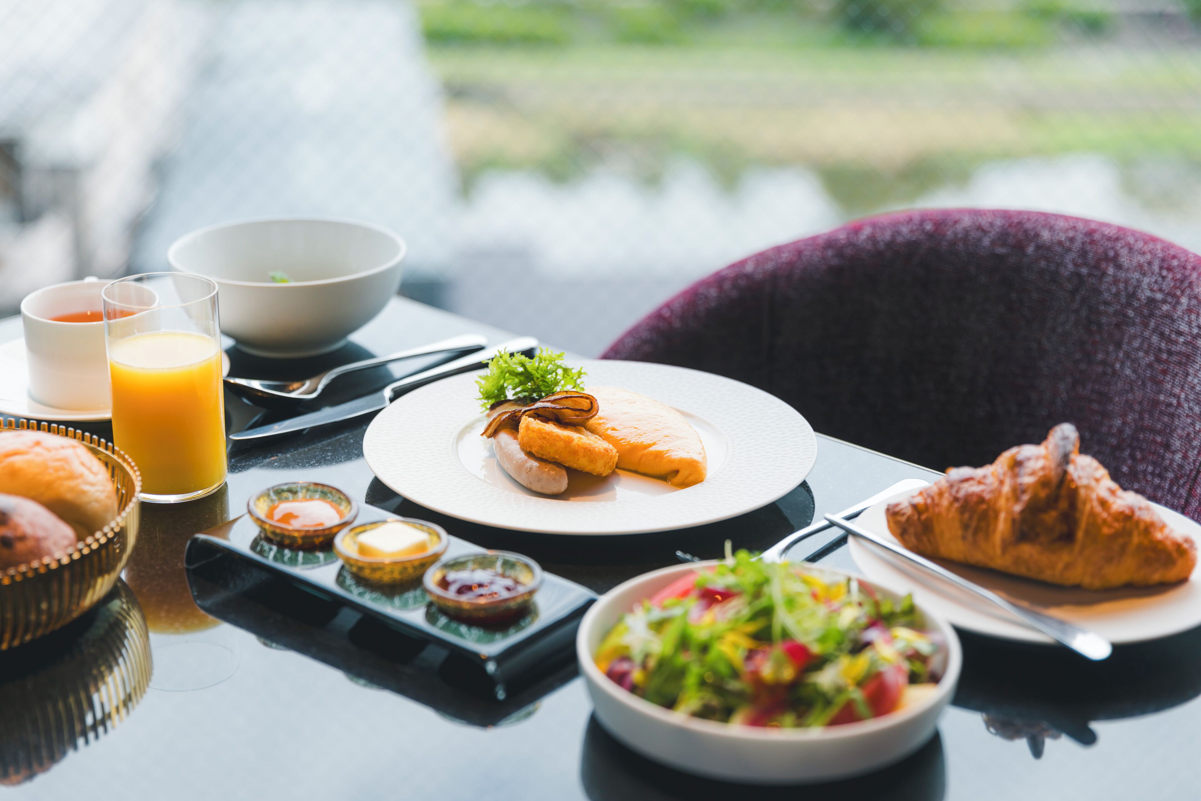 Une table de petit-déjeuner avec un croissant, une assiette de nourriture, un verre de jus d’orange et un bol de salade.