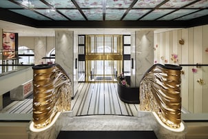Un moderno vestíbulo de hotel con suelo de mármol, un mostrador de recepción central y un techo de cristal con motivos florales.