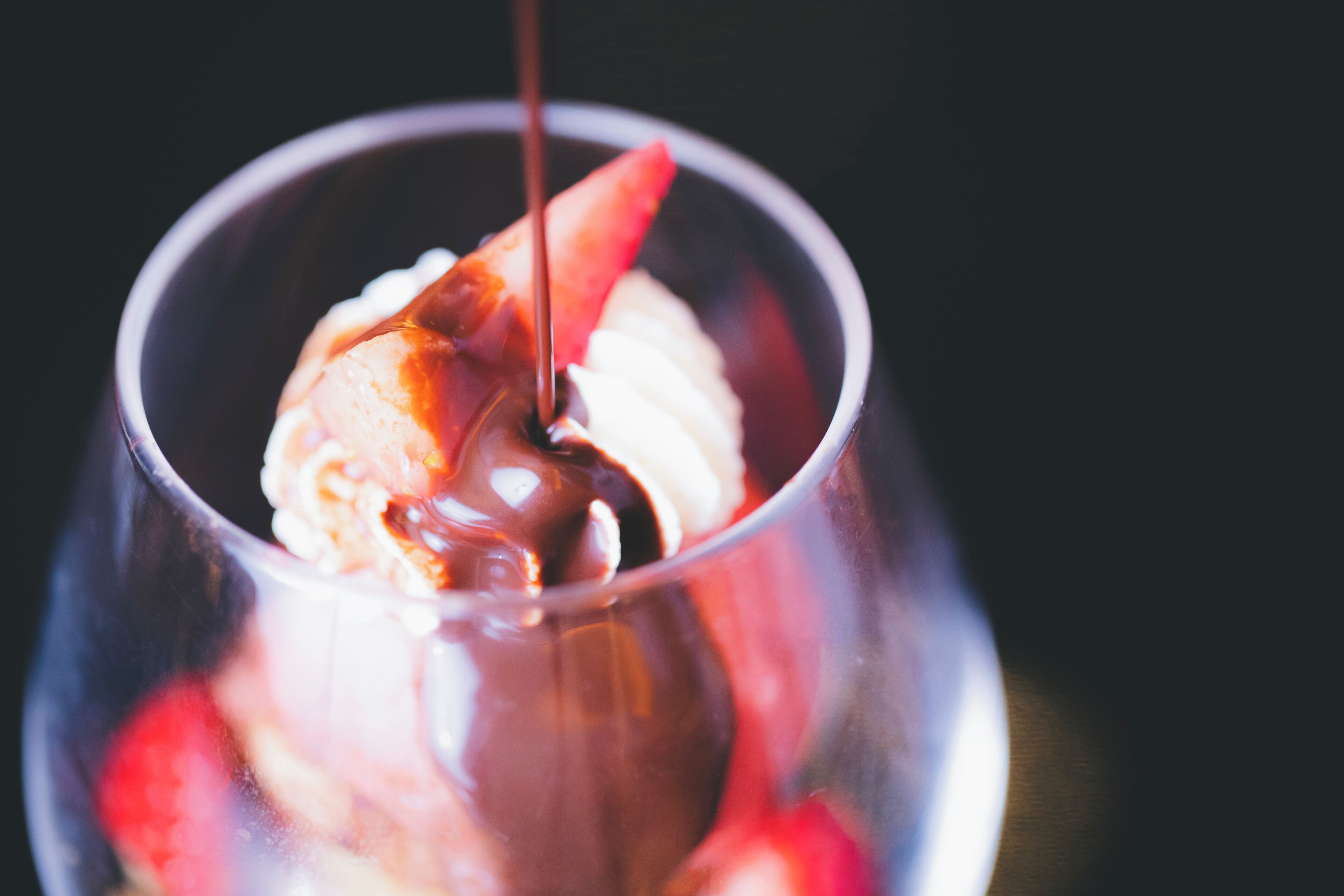 Postre en vaso con una bola de helado y salsa de chocolate vertida encima.