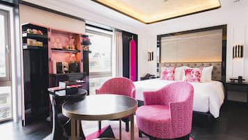 Een moderne hotelkamer met een groot bed, een bureau en twee roze stoelen.