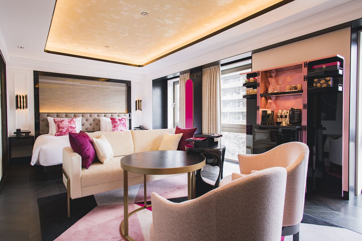 A modern hotel room with a bed, a sofa, a coffee table, and a minibar.
