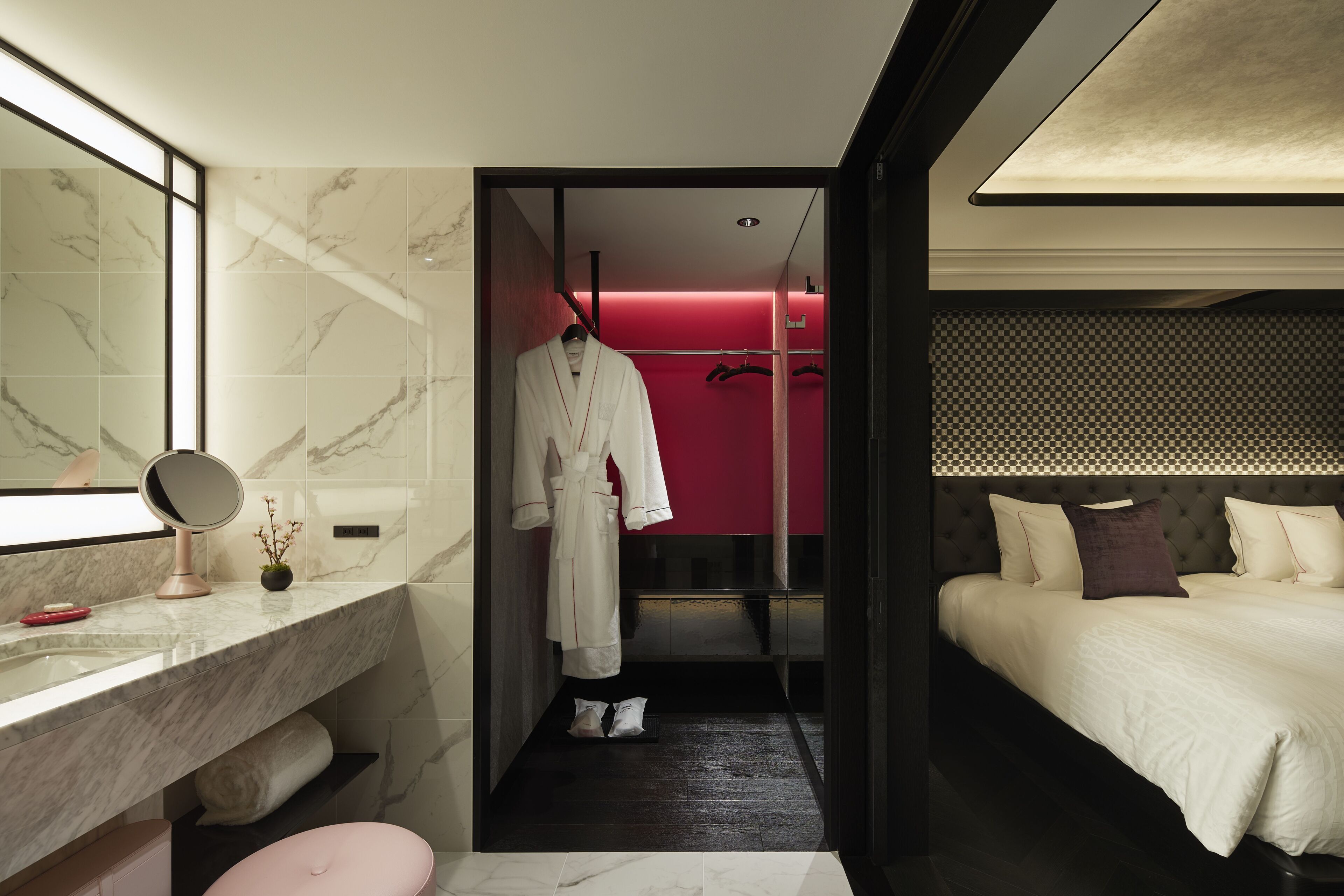 Habitación de hotel moderna con baño de mármol, cama con ropa de cama blanca y una pared de acento roja.