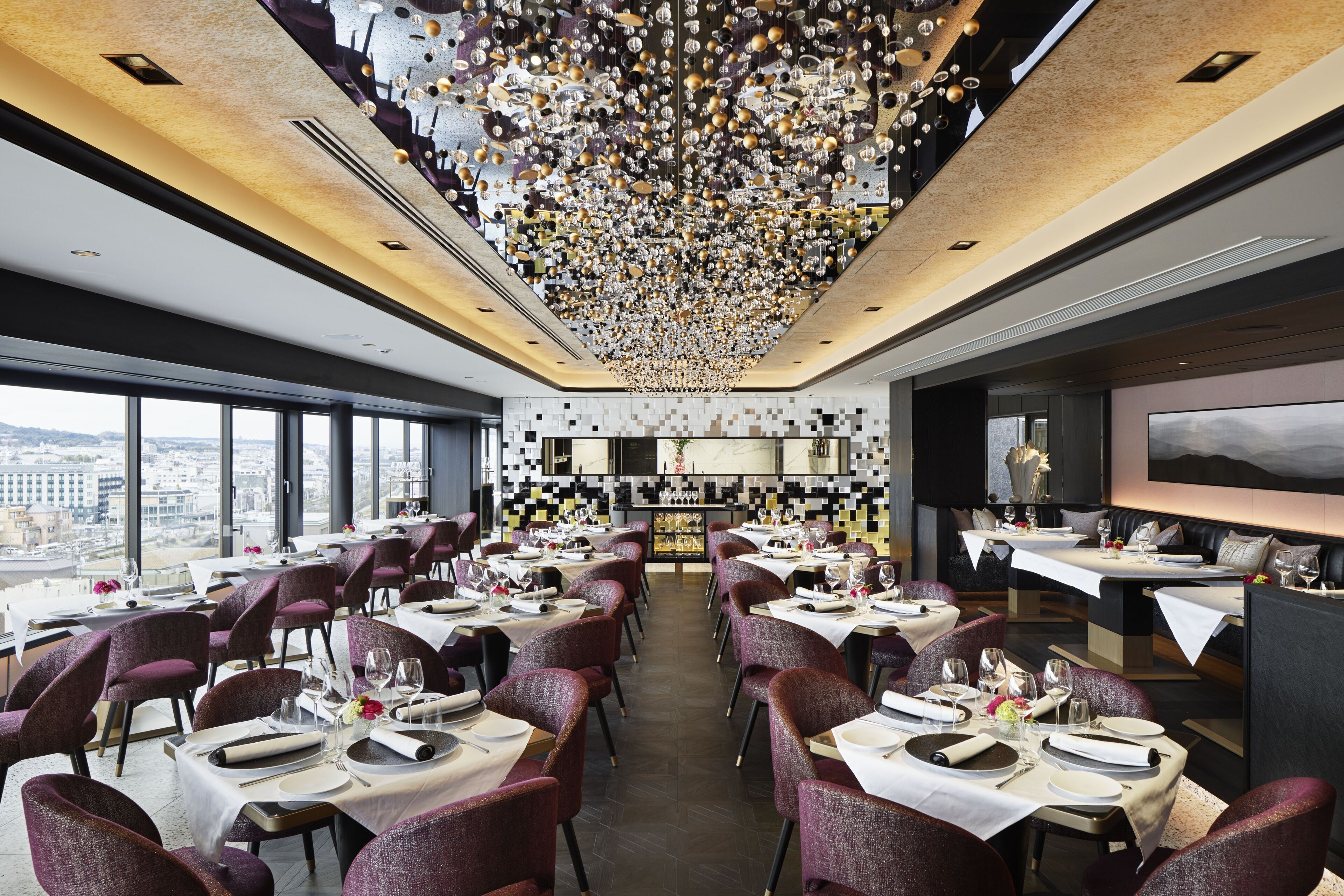 A modern restaurant with tables set for dining, a bar area, and a view of the city.