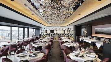 Un restaurante moderno con mesas dispuestas para comer, una zona de bar y vistas a la ciudad.