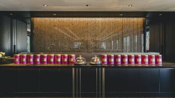 A reception area with a row of pink candles on a counter, a decorative wall with vertical elements, and a modern ceiling design.
