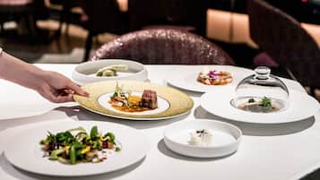 A table with various dishes, including a plate with a steak and vegetables, a bowl of soup, and a plate with a dessert.