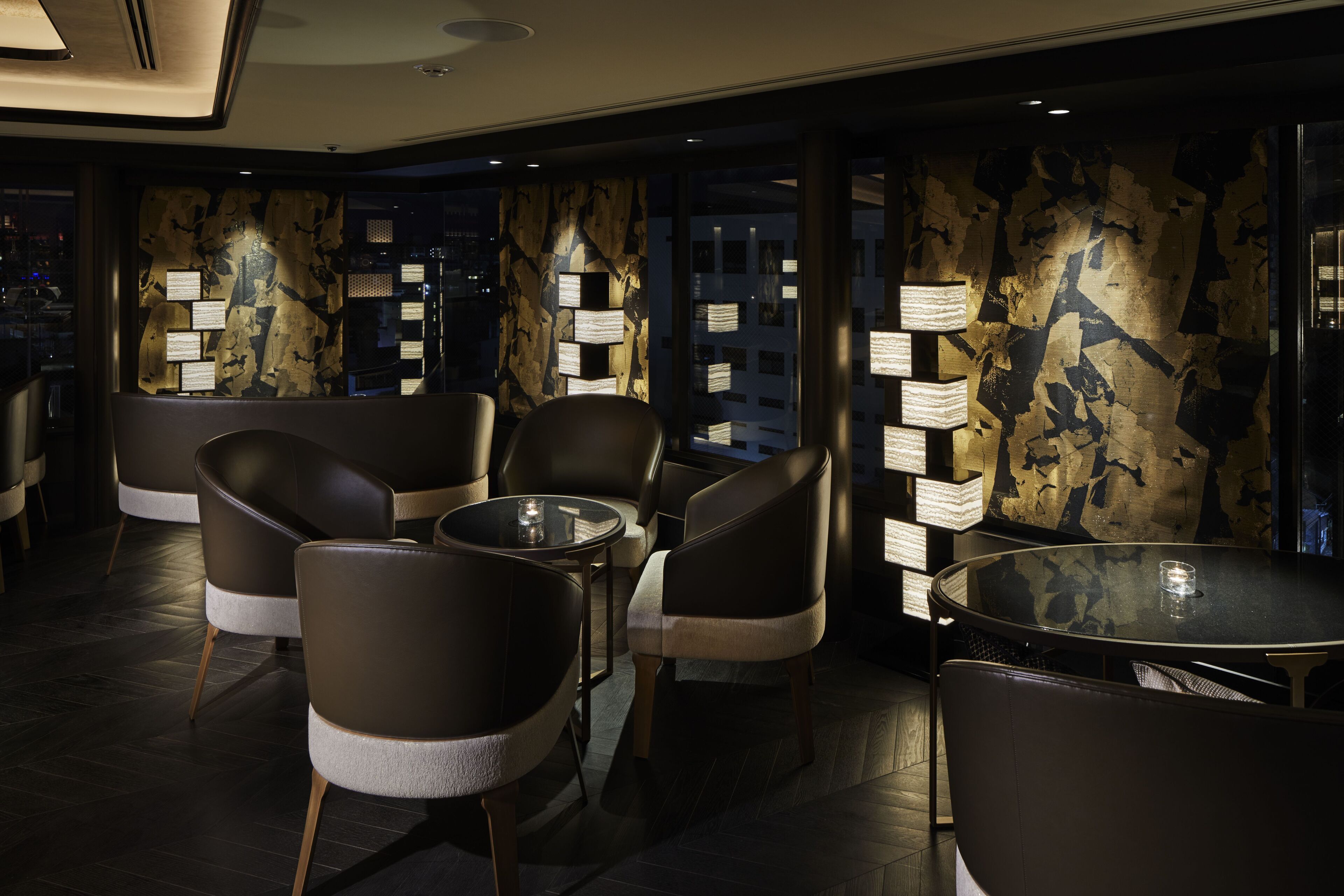 A modern interior with leather chairs, a glass table, and wall-mounted lamps.