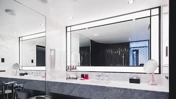 A modern bathroom with a large mirror, marble countertop, and a shower area visible through the glass door.