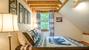 A cozy bedroom with a checkered bedspread, a wooden headboard, and a window with patterned curtains.