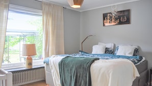 Un dormitorio con cama, un radiador, una ventana con cortinas, una lámpara y una obra de arte en la pared.