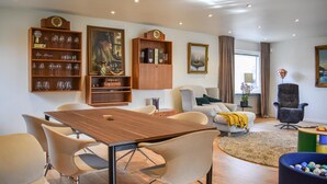 Un salón moderno con una mesa de comedor de madera, asientos cómodos y elementos decorativos como copas de vino y cuadros enmarcados.
