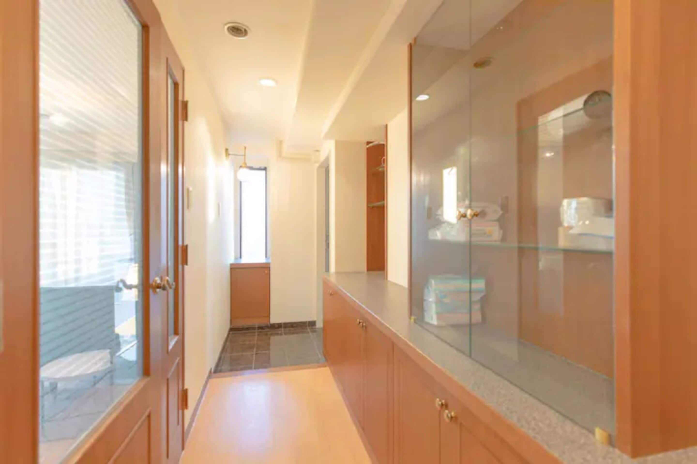 Un couloir avec des meubles de rangement en bois, une cabine de douche en verre et un sol carrelé.