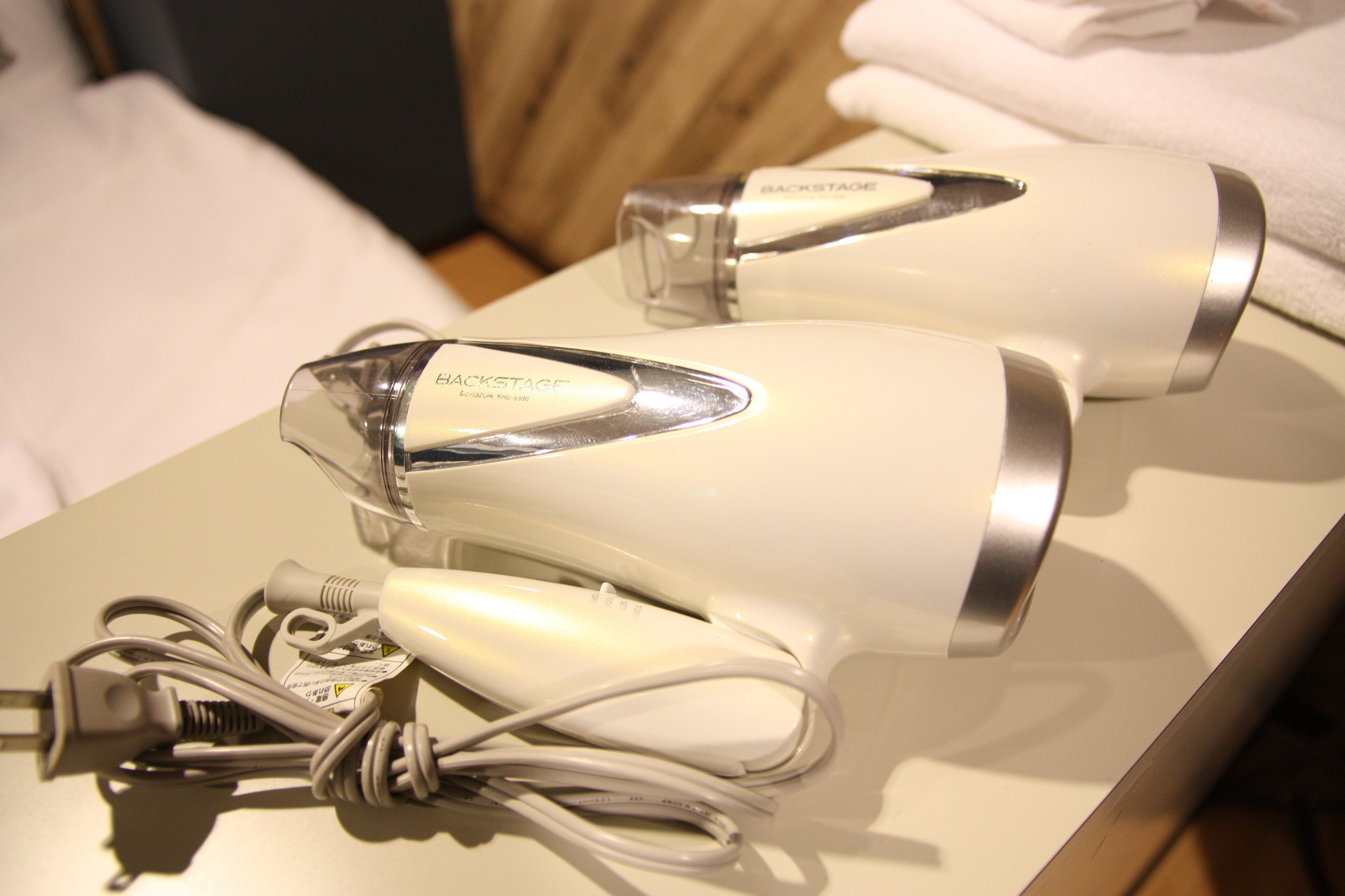 A hair dryer and its charging cable on a white surface.