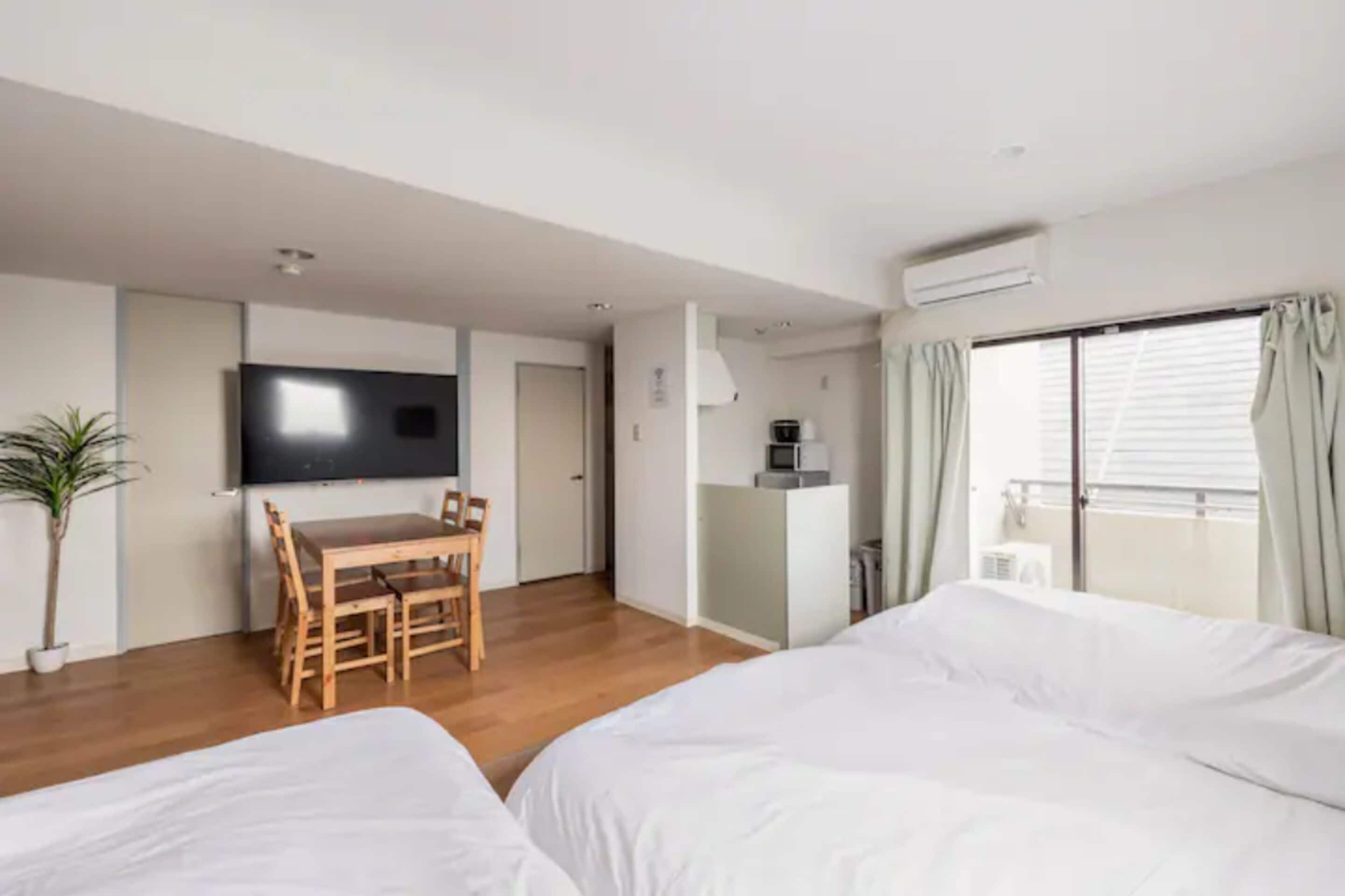 A modern hotel room with a large bed, a desk with a chair, a television, and a balcony with curtains.
