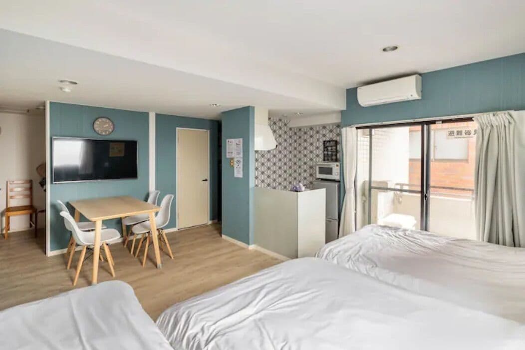 A hotel room with a bed, a desk with chairs, a television, a microwave, and a balcony with curtains.