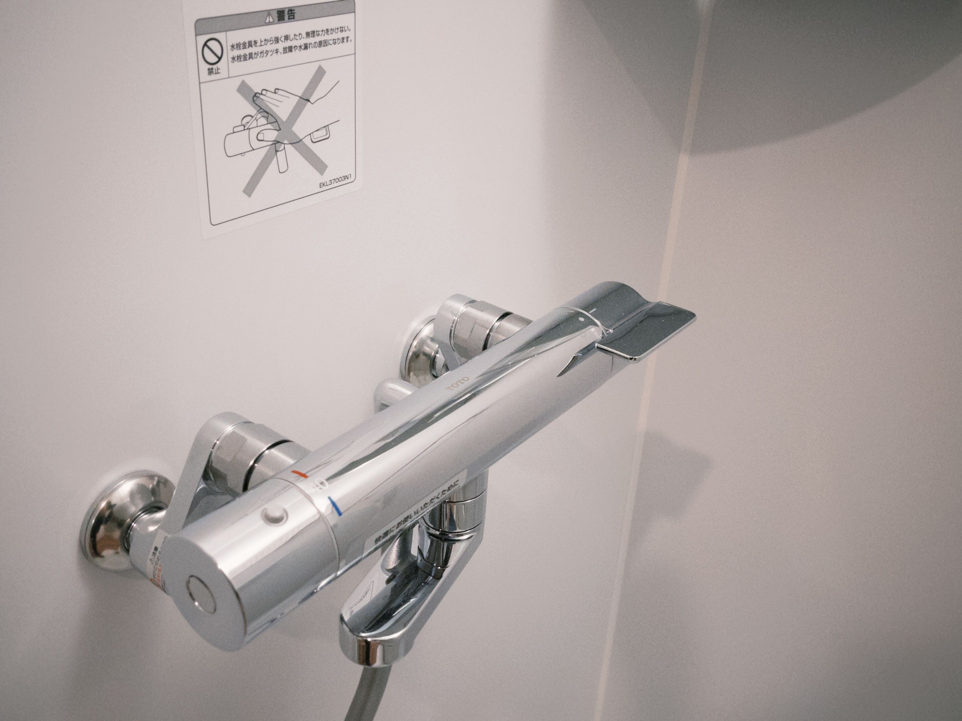 A chrome showerhead mounted on a wall with a warning sign above it.