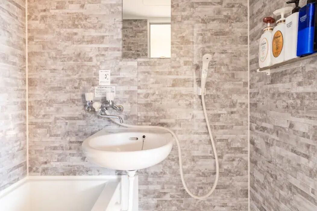 Un baño con lavamanos blanco, un espejo y cabezal de ducha.