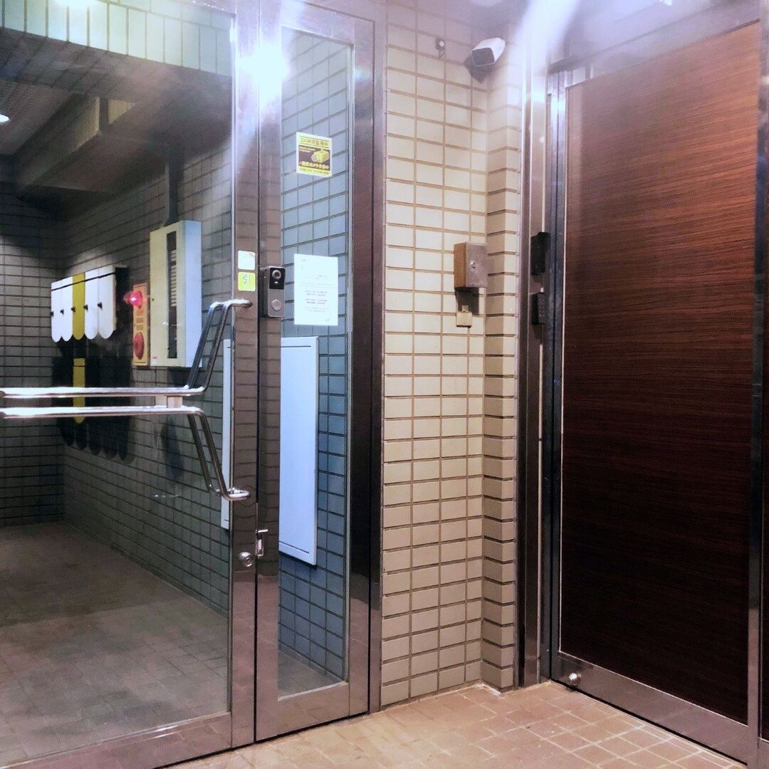 A hotel elevator with a glass door, a metal handrail, and a tiled wall.
