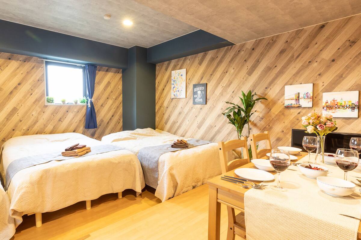 A room with two beds, a dining table set for four, and a window with curtains.