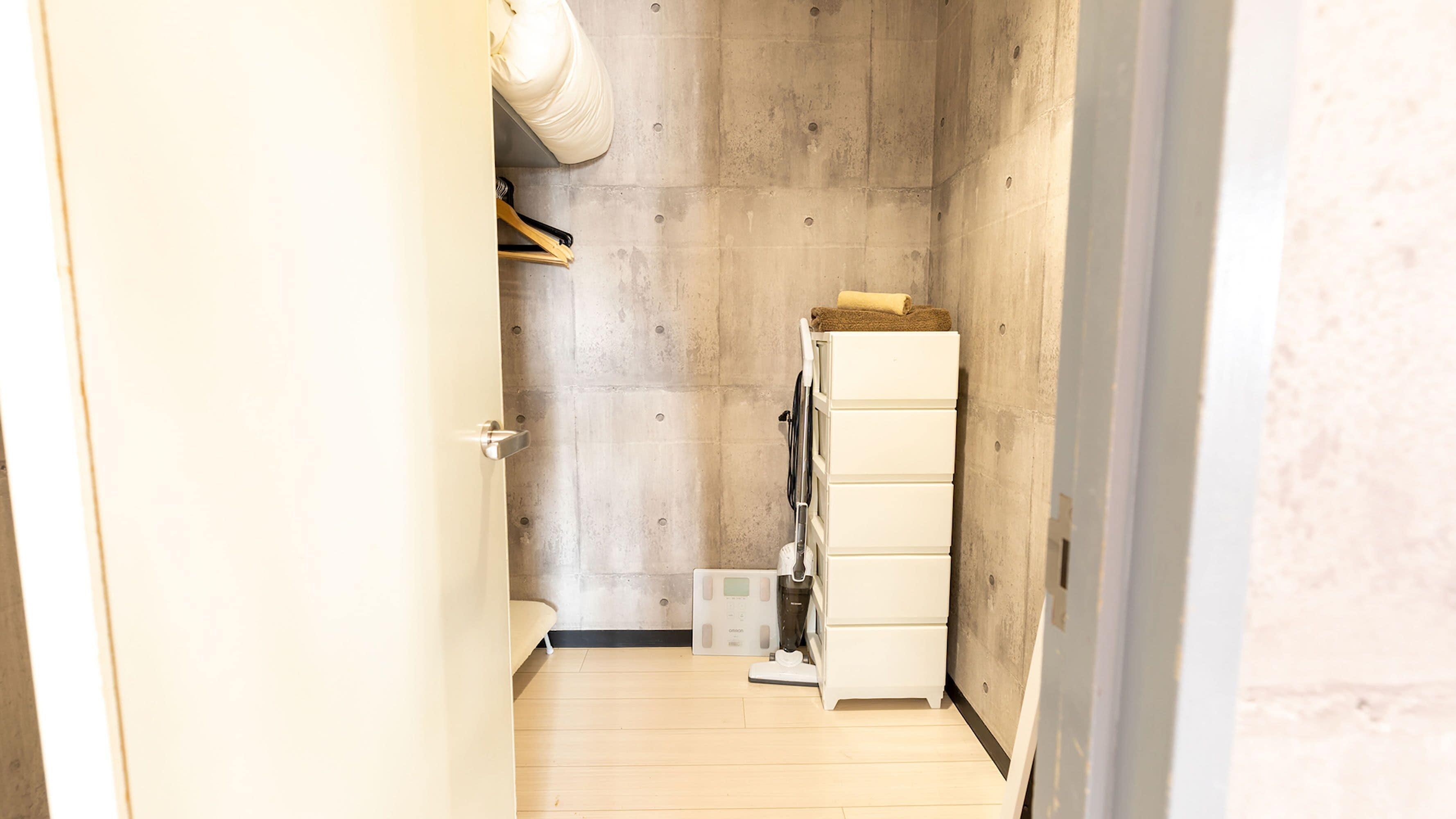 A narrow hallway with a concrete wall, a white door, and a white storage unit with a towel on top.