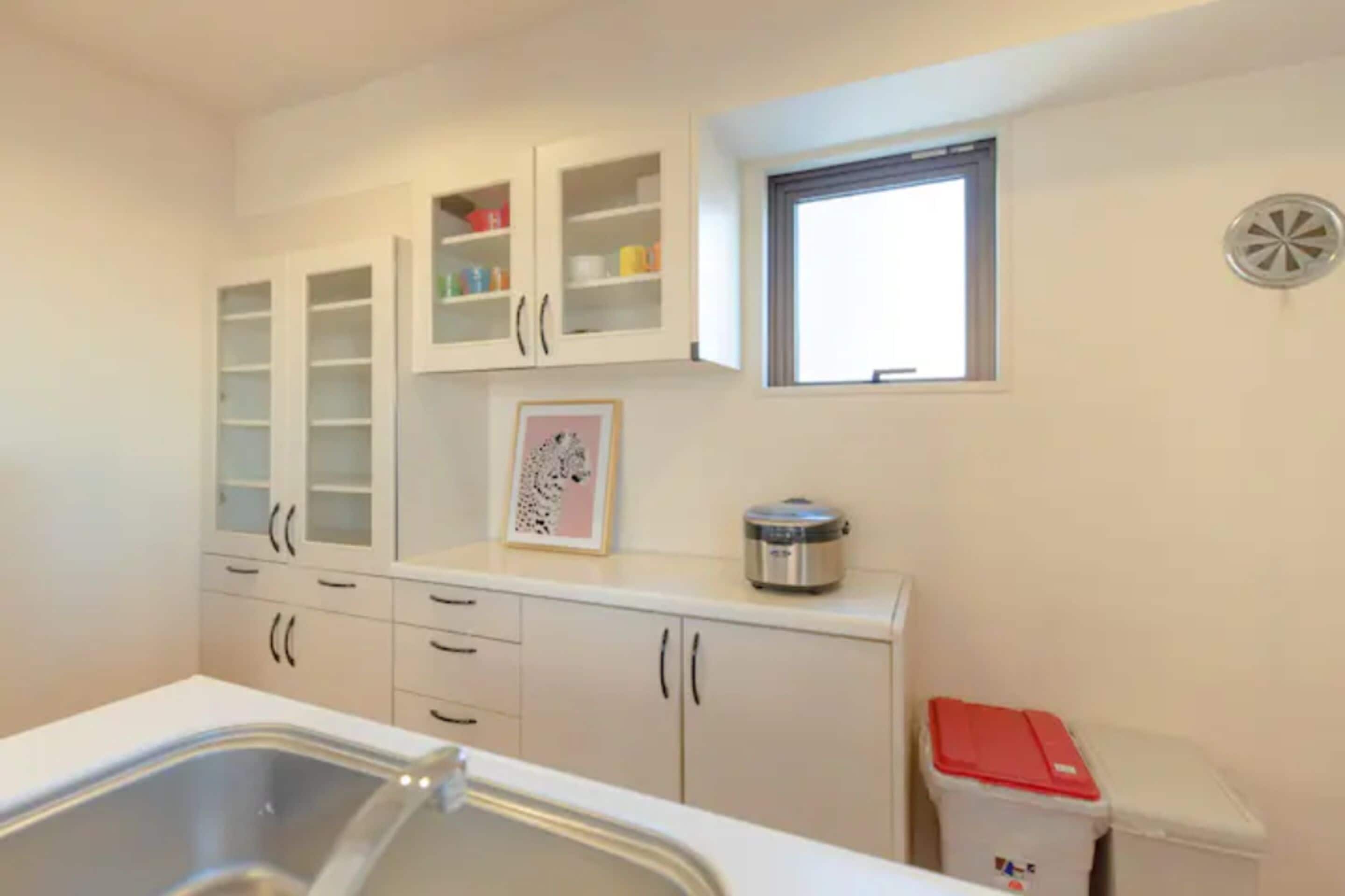 A kitchen with white cabinets, a stainless steel sink, a window, and a trash bin.
