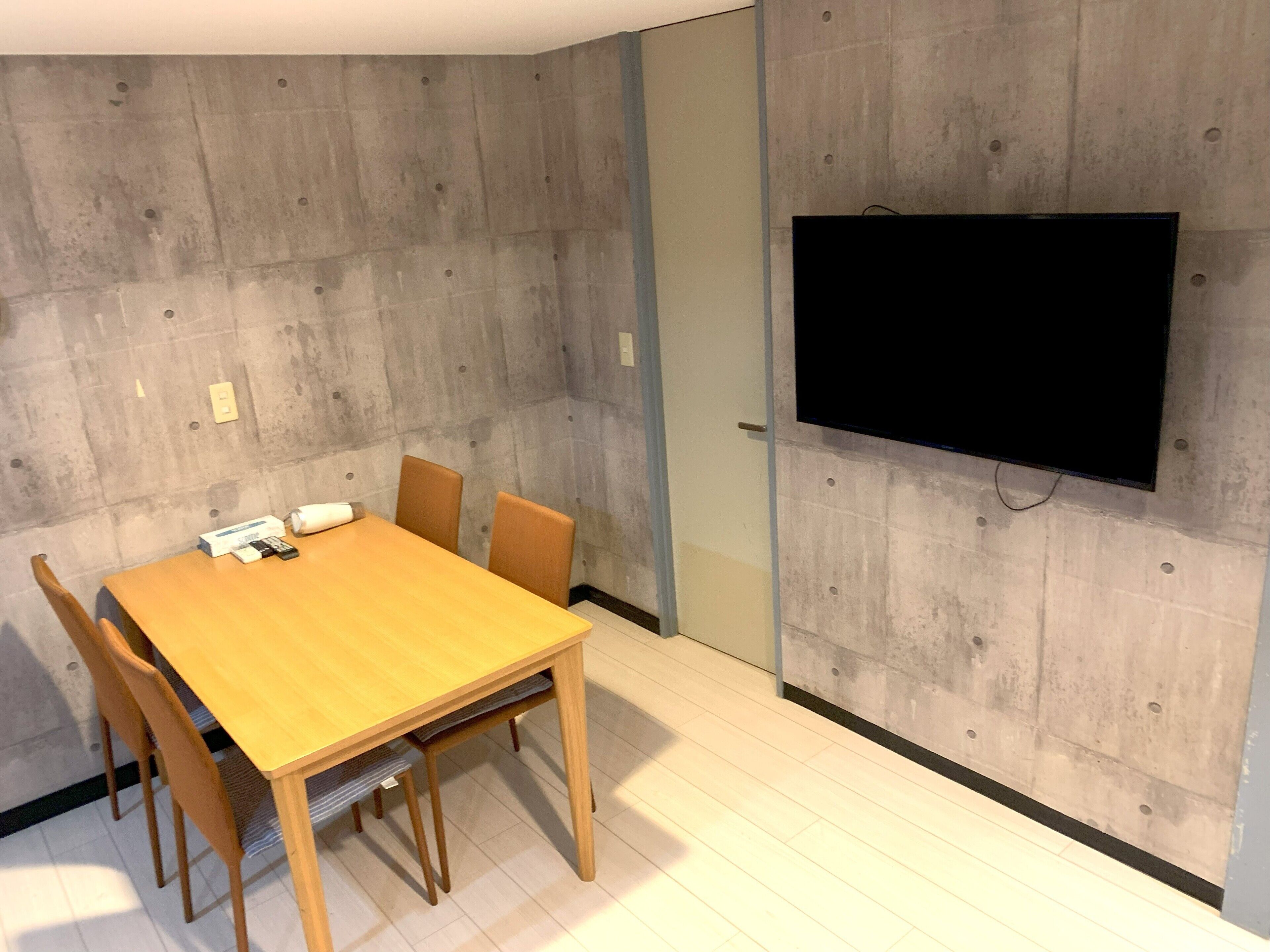 Une salle de conférence avec une table en bois, quatre chaises, un téléviseur à écran plat fixé au mur et une porte dotée d’un interrupteur.