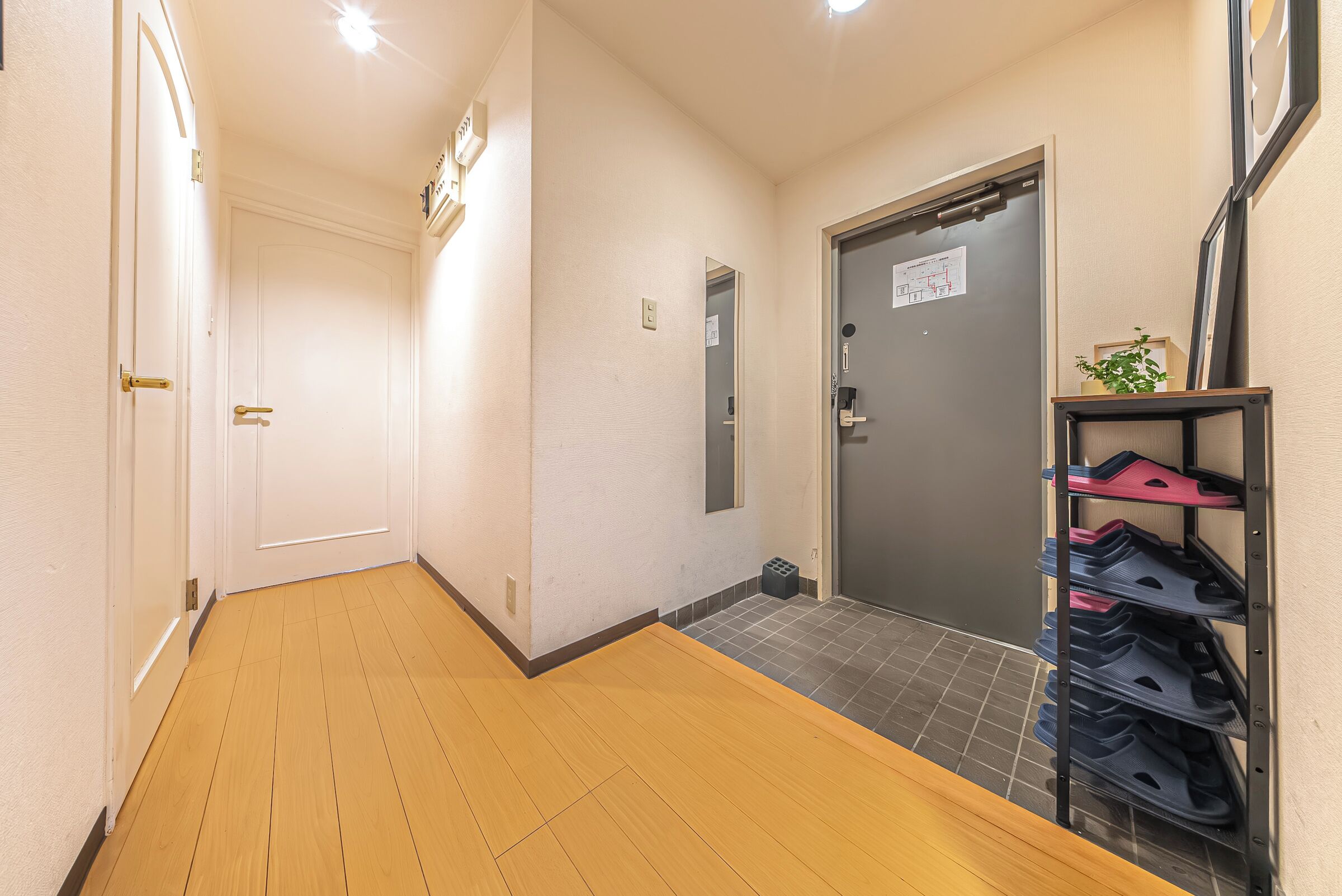 A hallway with a wooden floor, a shoe rack, and a door with a map on the wall.