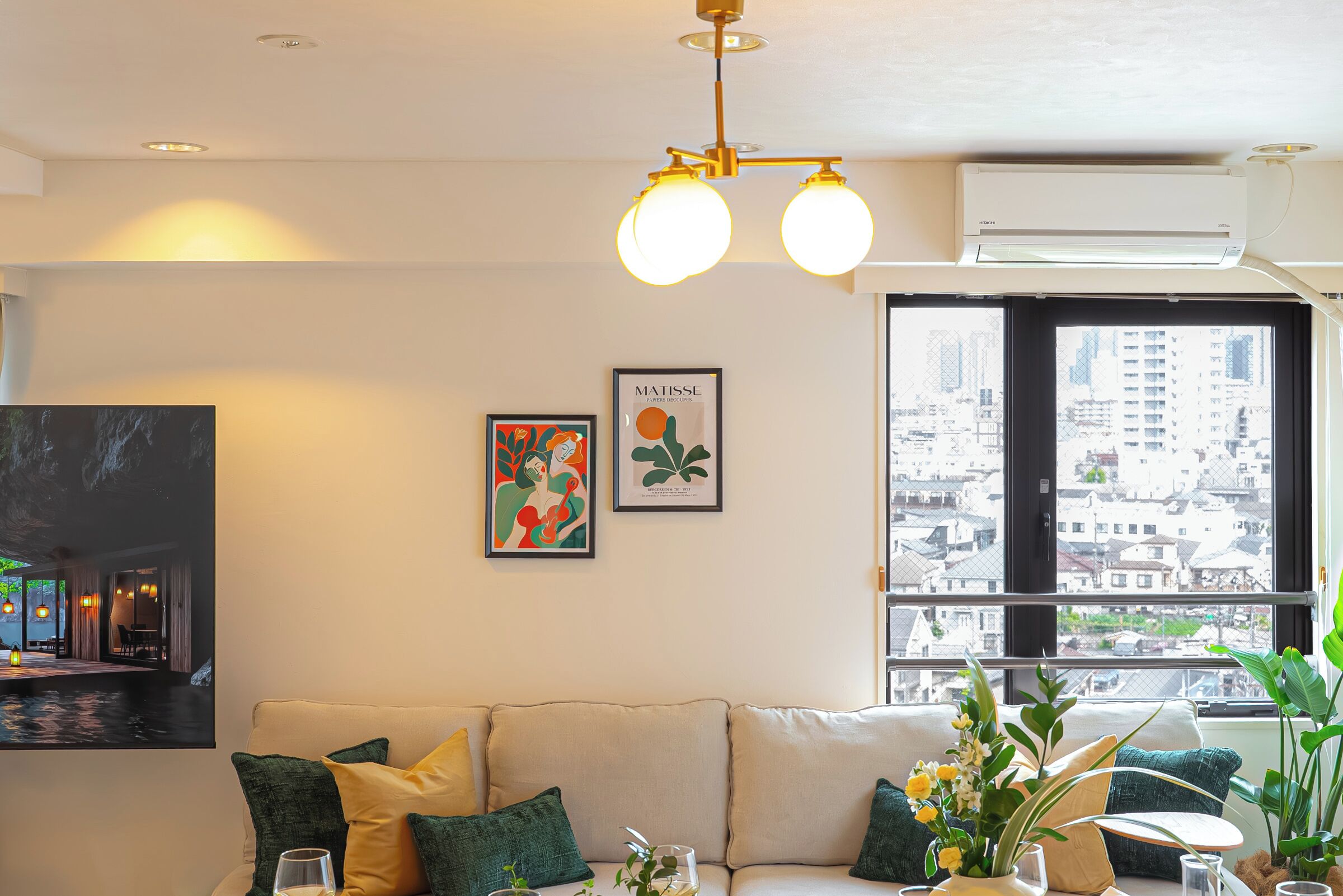 A living room with a sofa, a coffee table, a painting, and a window with a city view.