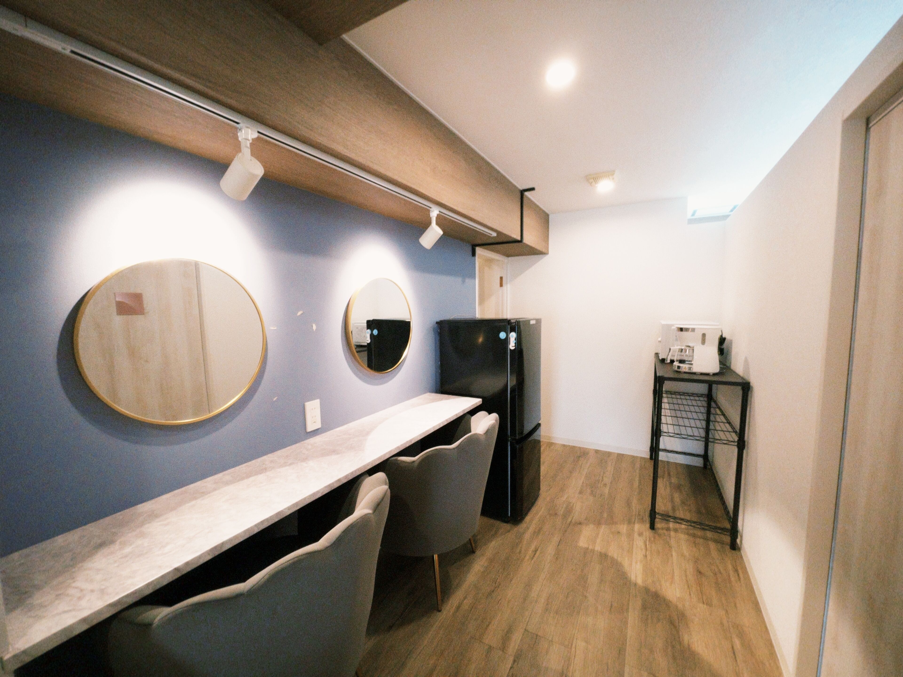 Una kitchenette compacta con mostrador, dos sillas, un refrigerador y una pequeña mesa con cafetera.
