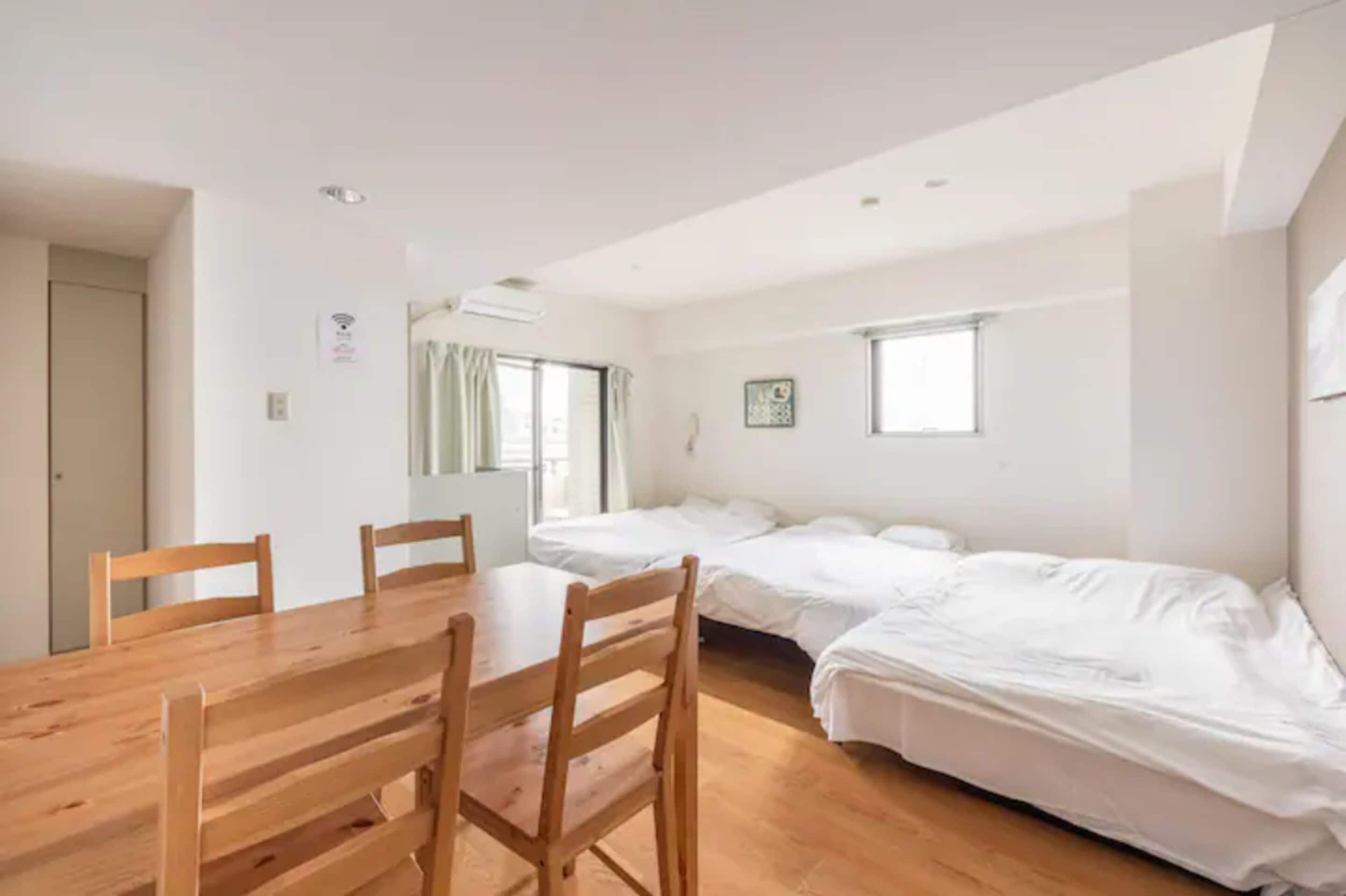 Una habitación con una mesa de comedor de madera y sillas, dos camas individuales, una ventana y una puerta.