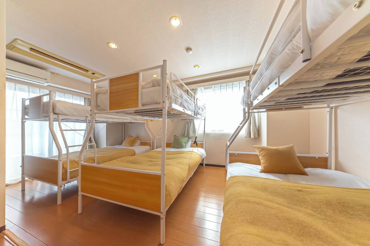 A bunk bed room with a wooden floor, white walls, and a window with curtains.