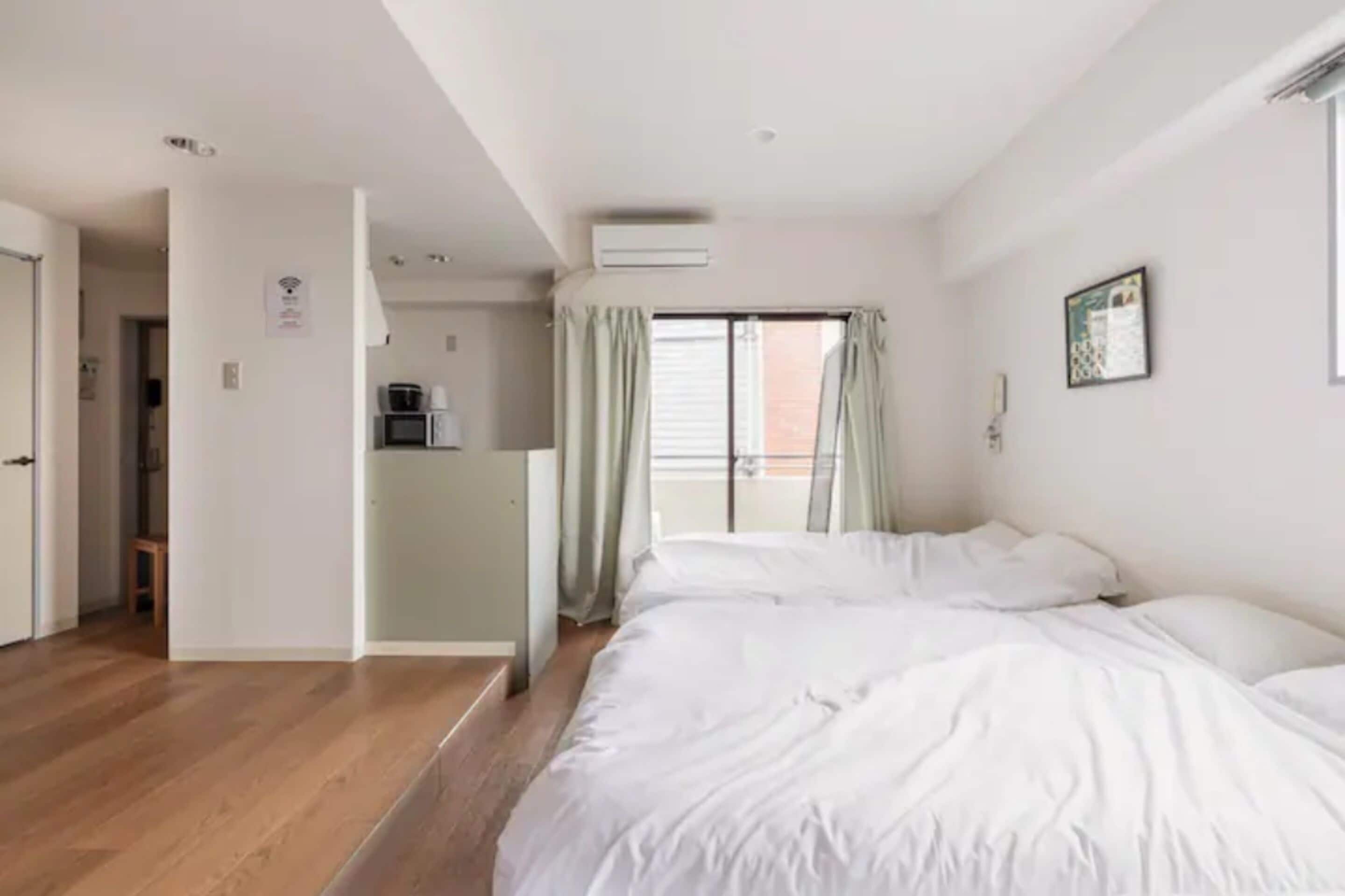 A bedroom with a large bed, a kitchenette, and a sliding door to a balcony.