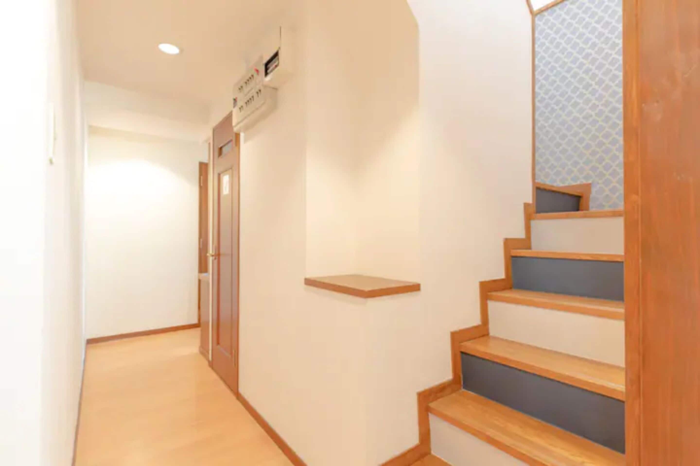 A narrow hallway with wooden steps leading to a landing, a door on the left, and a wall-mounted air conditioning unit.