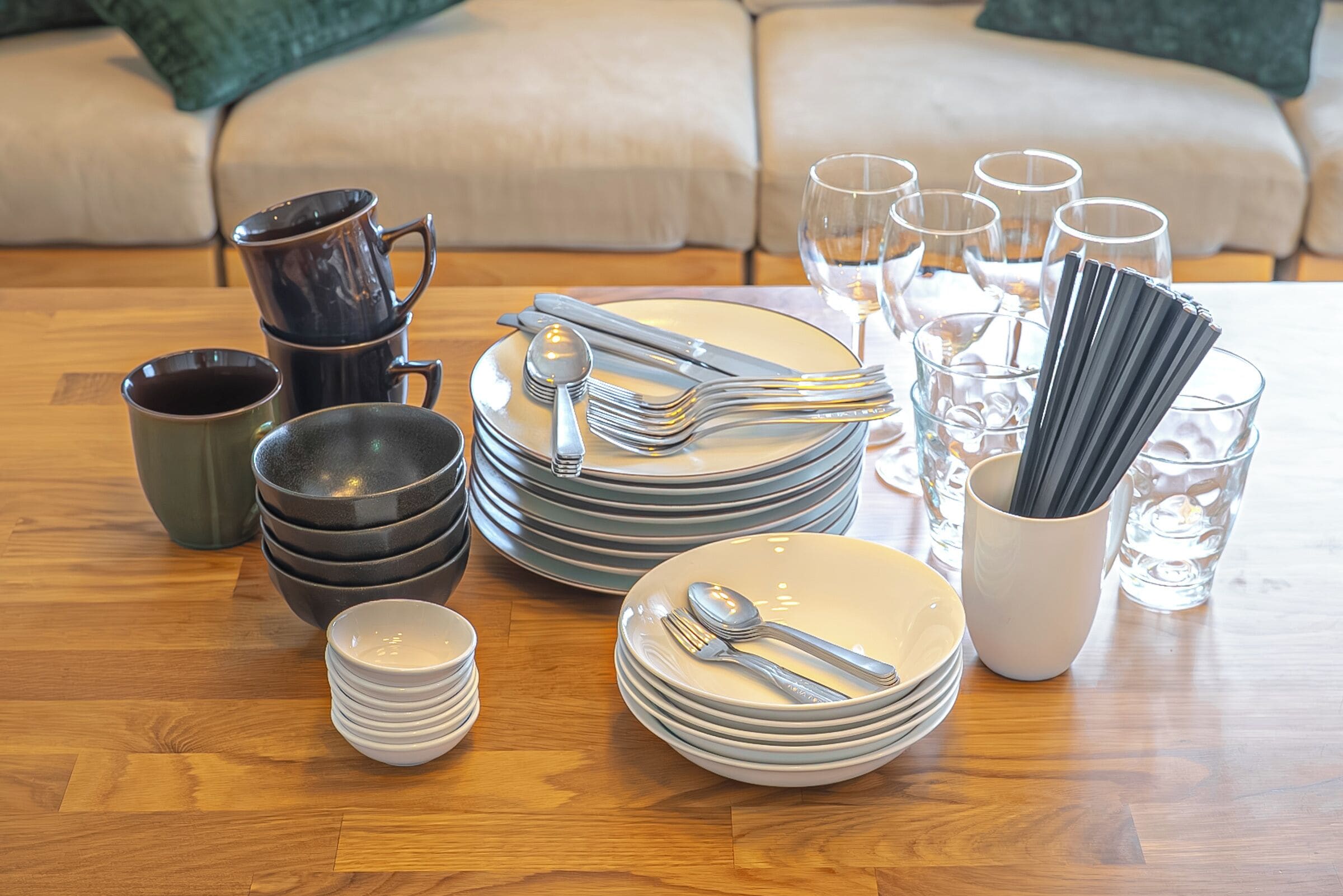 A dining setup with stacked plates, cutlery, and glasses on a wooden table.