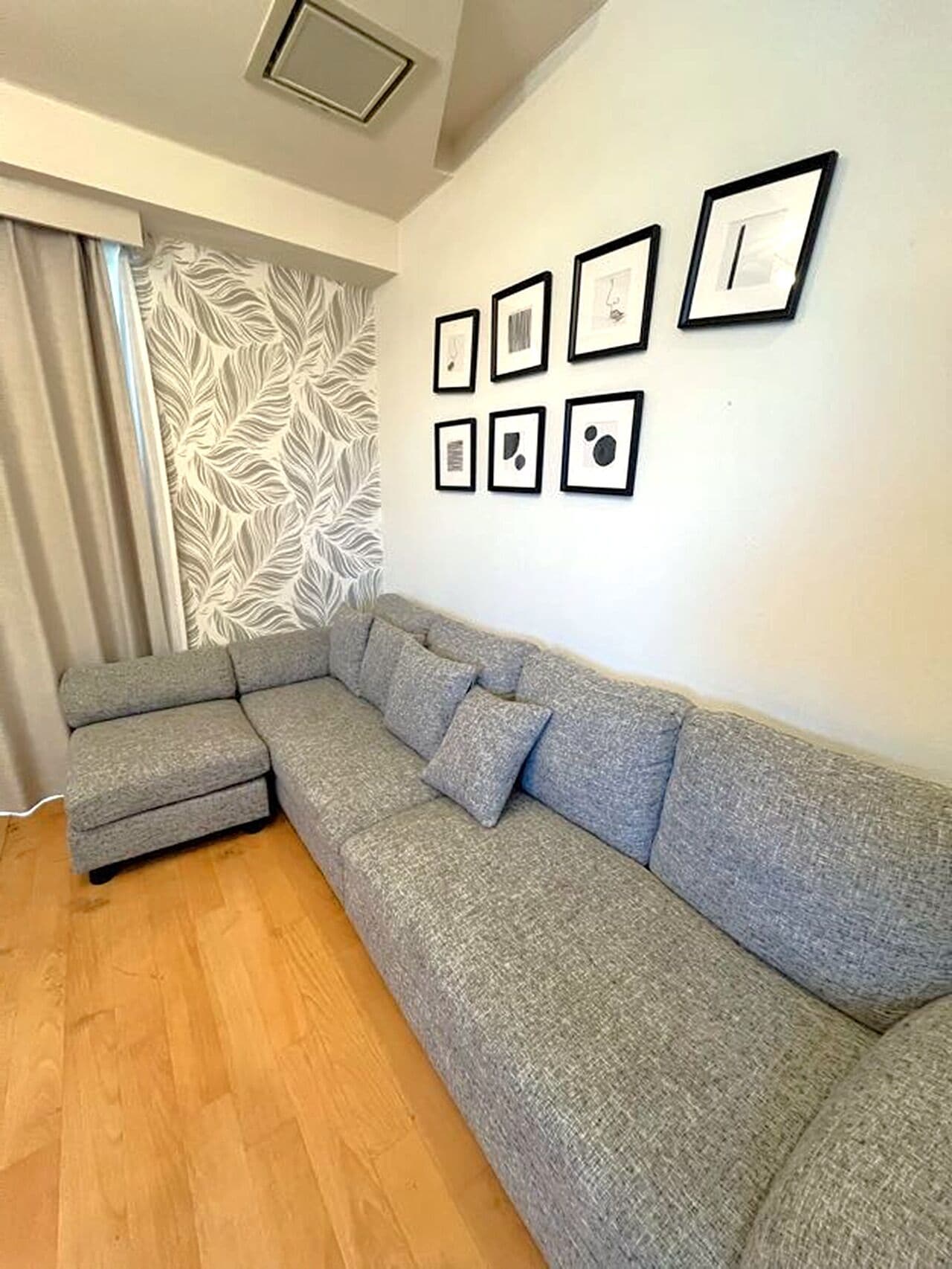 A modern living room with a grey sectional sofa, a patterned wallpaper, and a series of framed pictures on the wall.