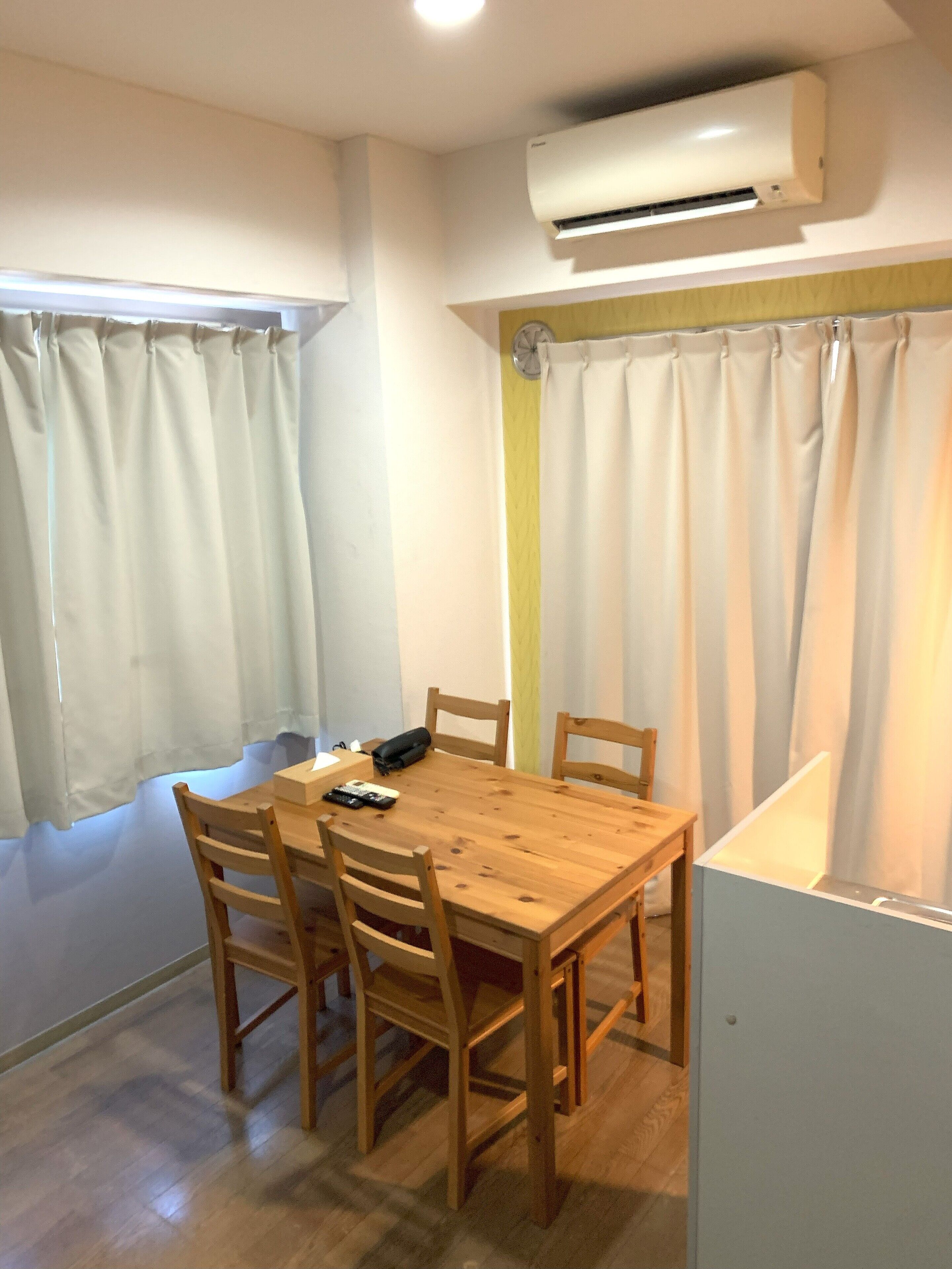 A dining area with a wooden table and chairs, an air conditioner, and a window with curtains.