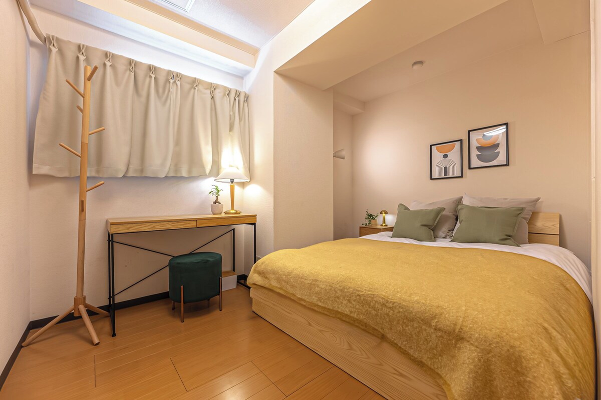 Une chambre à coucher comprenant un lit, un bureau, une chaise, une lampe et deux tableaux encadrés accrochés au mur.