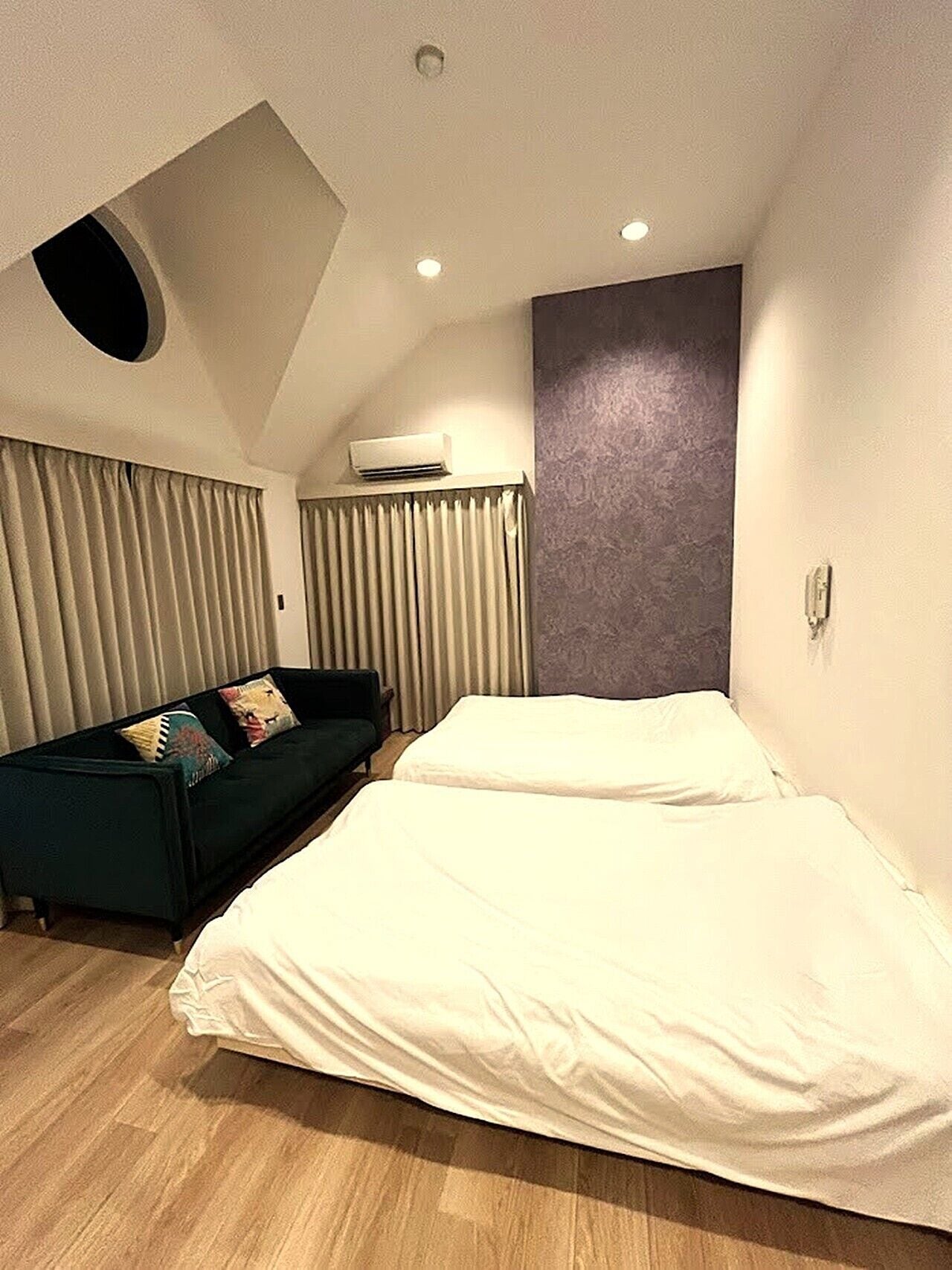 A modern hotel room with a bed, a sofa, and a ceiling light fixture.