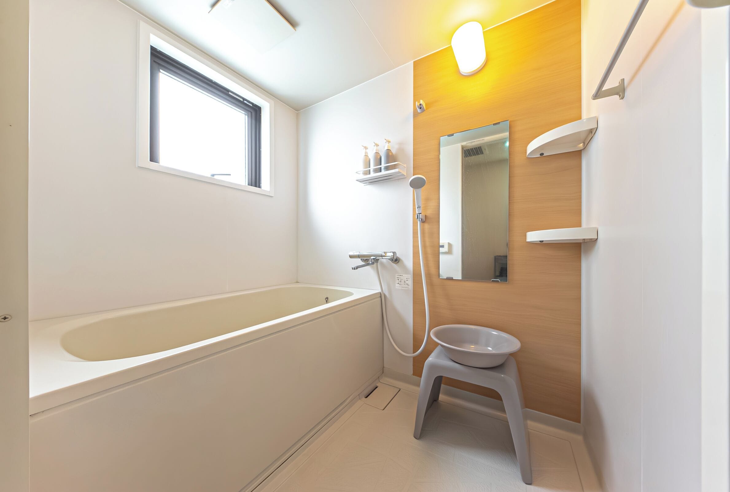 Un baño moderno con una bañera, un taburete pequeño, un espejo y un estante con artículos de aseo.