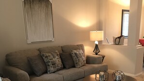 Uma sala de estar com um sofá cinzento, uma mesa de centro redonda e uma luminária.