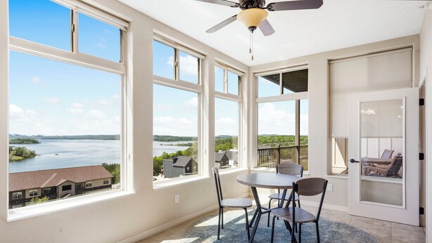 Una habitación con ventanas amplias con vistas a un lago, un ventilador de techo y un comedor con sillas y una mesa.