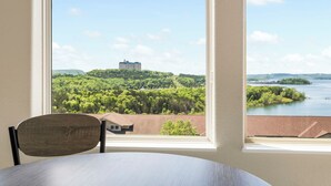 Habitación con un ventanal amplio que ofrece vistas a un edificio en una colina, un cuerpo de agua y vegetación circundante.